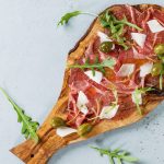 Beef carpaccio on olive wood serving board with capers, olive oil cheese and arugula, served over blue stone texture background. Top view with space for text.